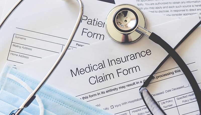 A stethoscope and surgical mask are on top of a few forms marked “Medical Insurance Claim Form.”