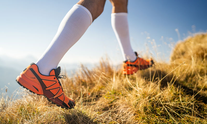 Person in sneakers and compression socks walking up a grassy incline