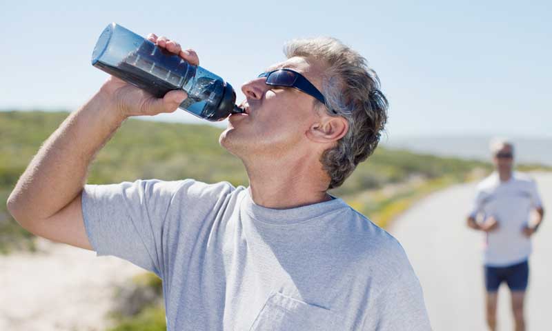 A man running along the beach stops to drink water