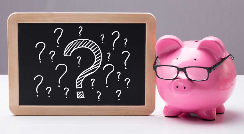 A pink piggy bank with eyeglasses sitting next to a miniature blackboard with question marks written on it