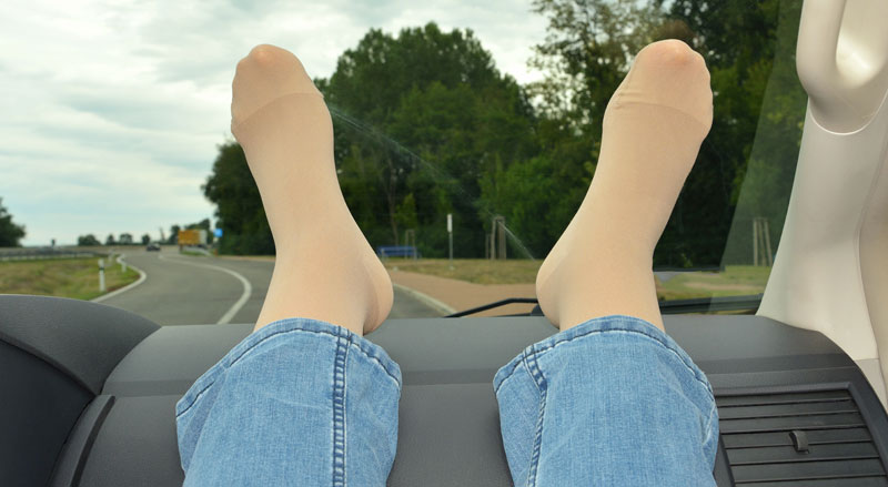 A car passenger’s wearing compression socks with legs elevated on the dashboard