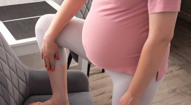 A pregnant woman is looking at her raised lower leg