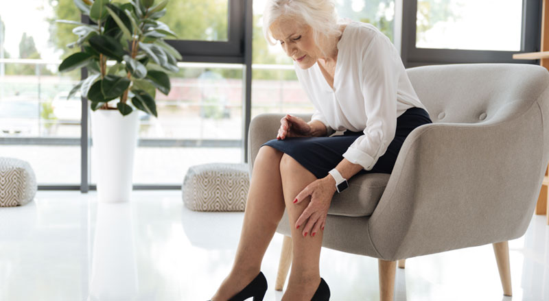 An older woman in a chair rubbing her painful leg.