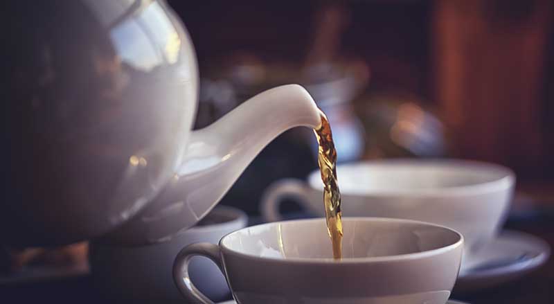 Pouring tea from a white teapot into a cup with saucer 