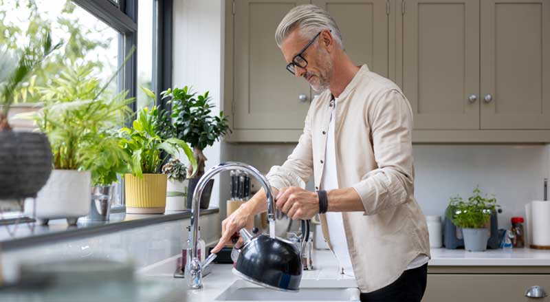 A man filling a tea kettle with water at his kitchen sink