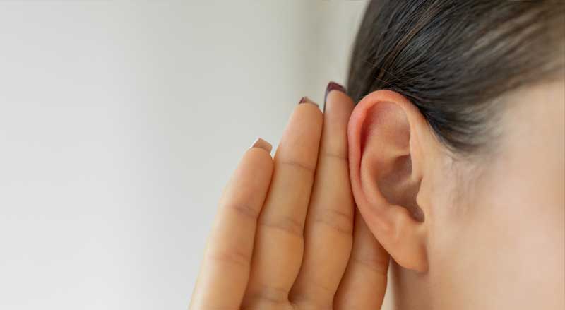 Close-up of a woman’s hand behind her ear to help hearing